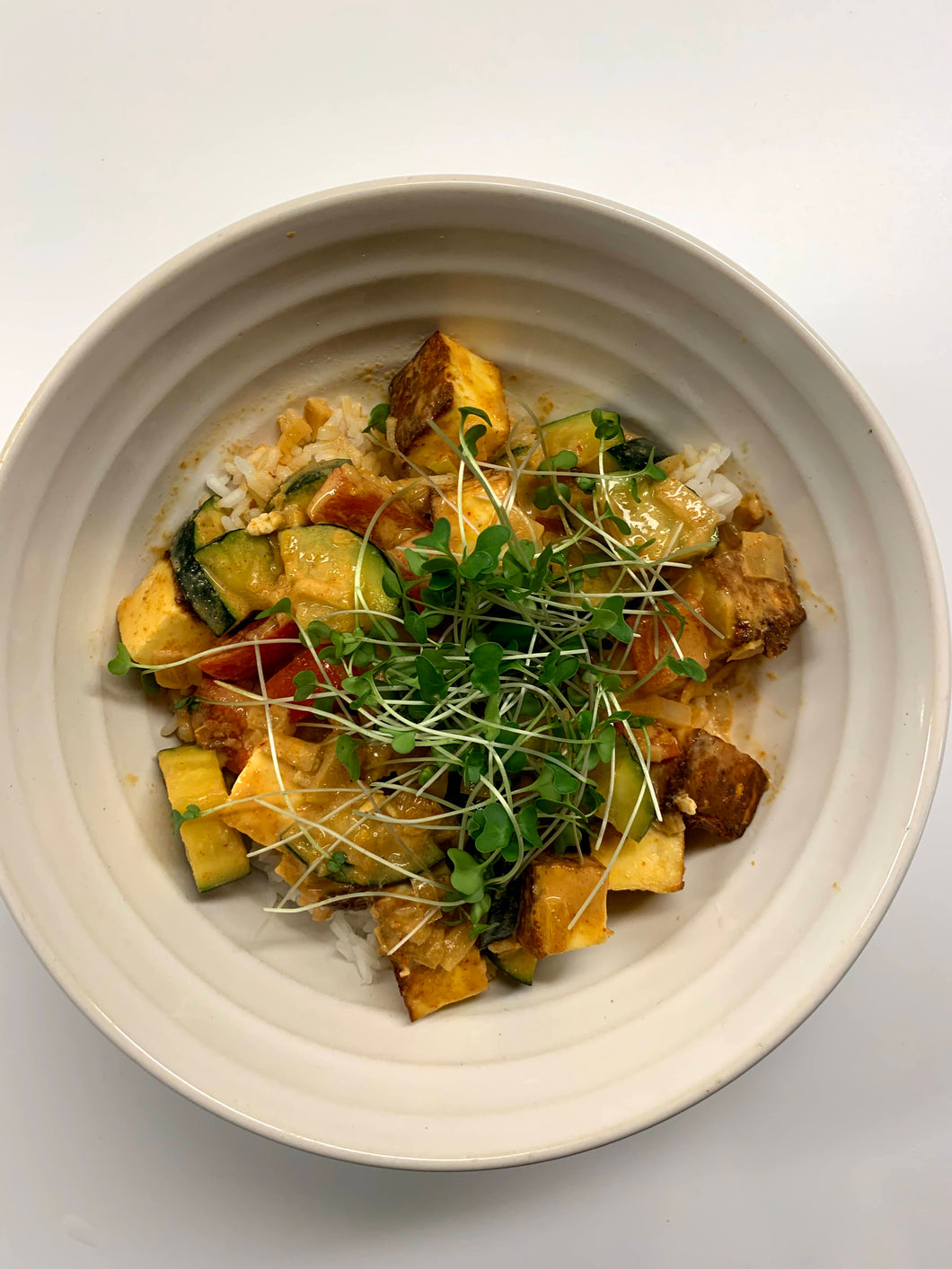 A bowl of green curry paneer topped with broccoli microgreens.